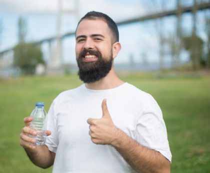 Cheerful man with a beard giving thumbs up while holding a water bottle in a park setting in Portugal.
