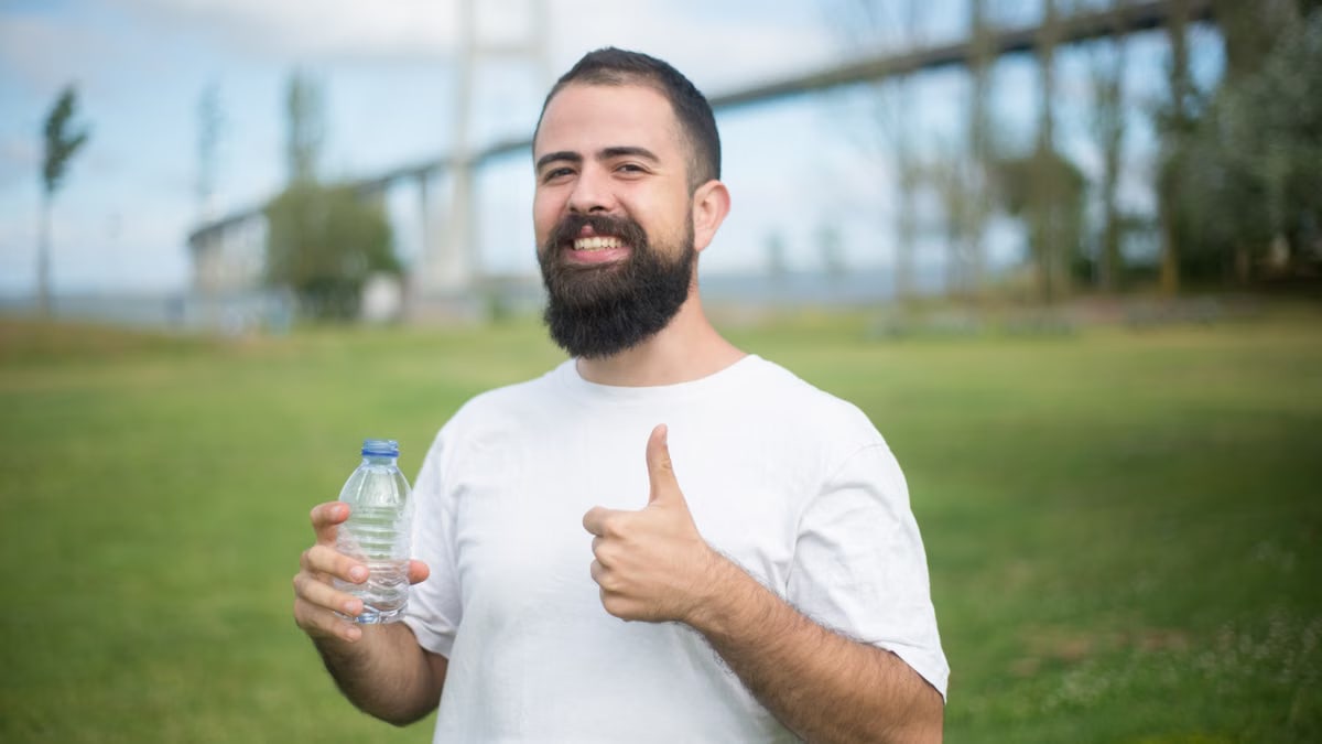 Cheerful man with a beard giving thumbs up while holding a water bottle in a park setting in Portugal.