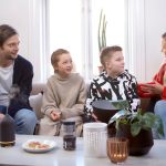 A family of four converse in a living room while a black volant diffuser is on the table.