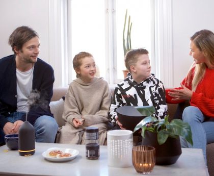 A family of four converse in a living room while a black volant diffuser is on the table.